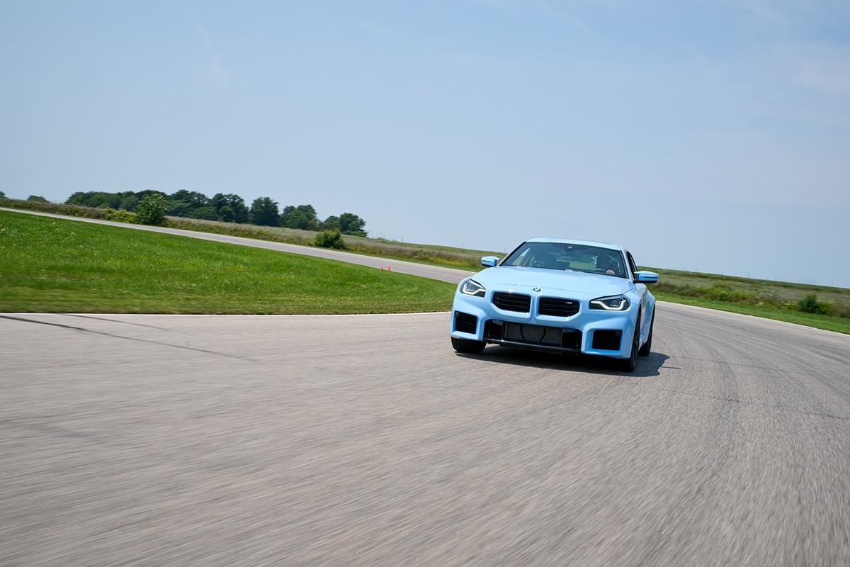 Light blue 2024 BMW M2 driving around a curve on the track