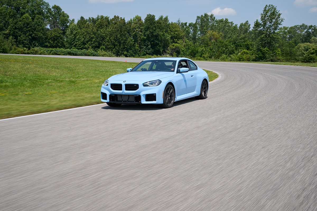 Light blue 2024 BMW M2 driving around a curve on the track